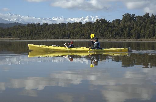 Sea kayaking on Okarito Lagoon in New Zealand. Nnote the snow on the peaks.